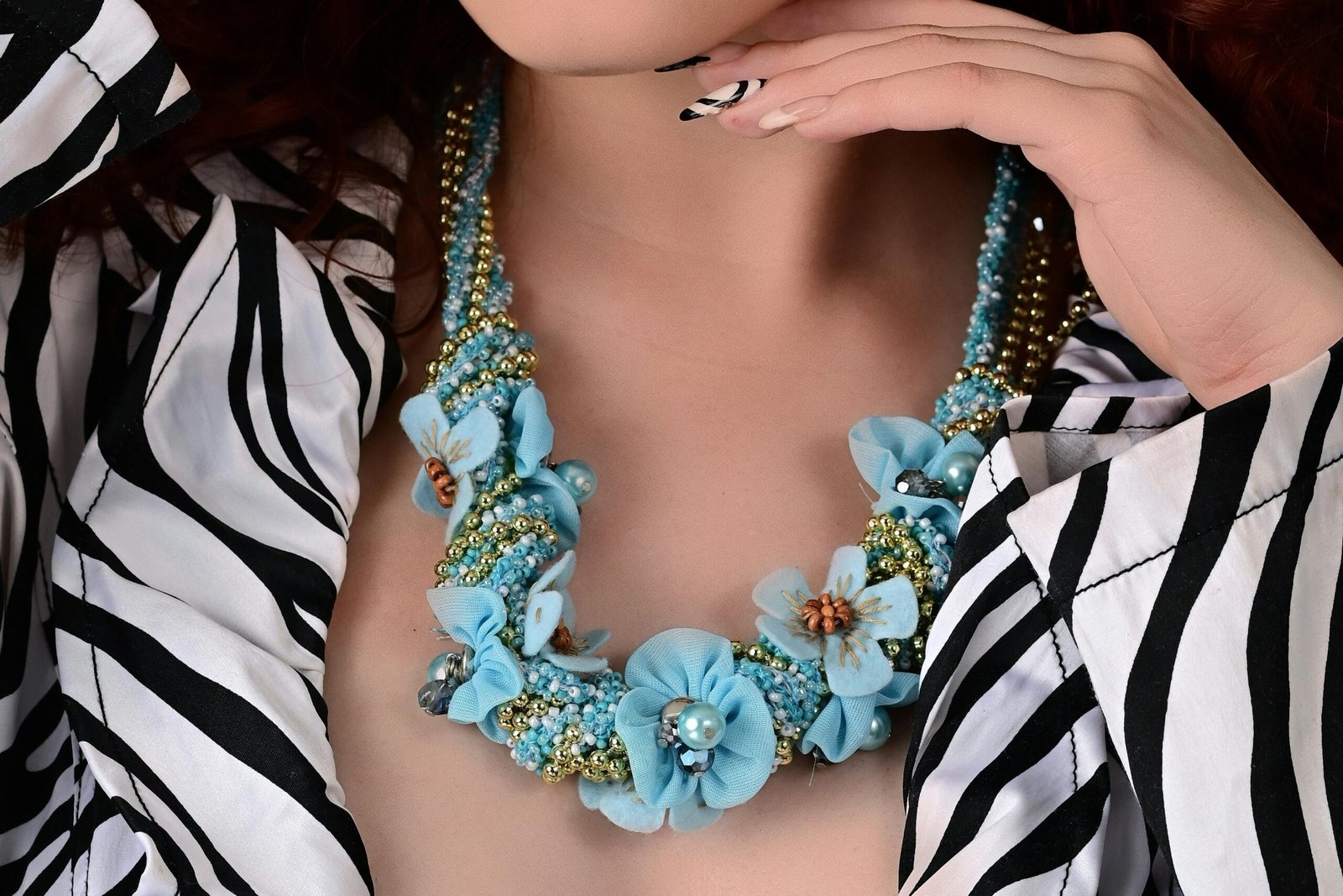 A view of the bottom of a woman's chin, neck, and part of her blouse. She has her left hand under her chin and is showings a fingernail polished in a zebra-print pattern. She is wearing a necklace made of light blue flowers and beads. She is also wearing a black and white, zebra-print blouse.